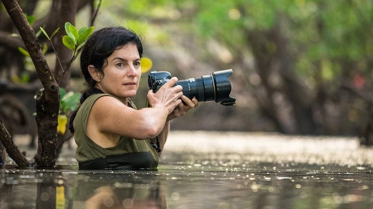 Ami Vitale, waist-deep in water, holds her camera, looking for the next shot. - photo