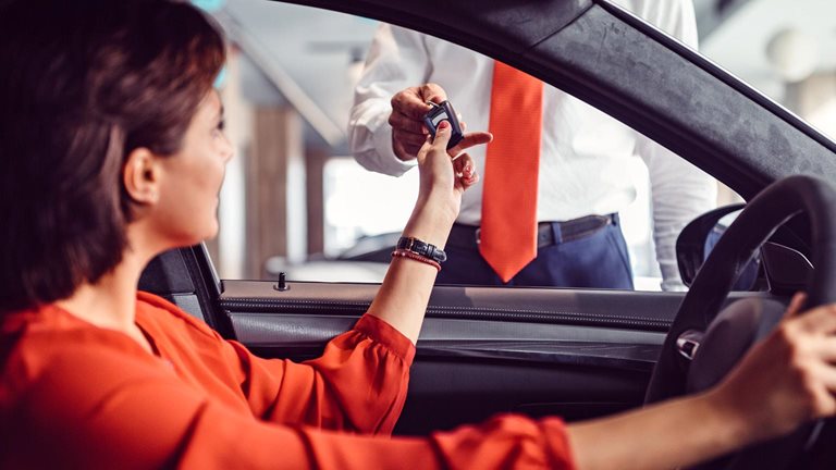 Woman in car handing car keys to a man standing outside