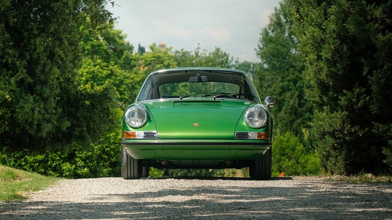 Classic green Porsche sitting on road, trees in the background.
