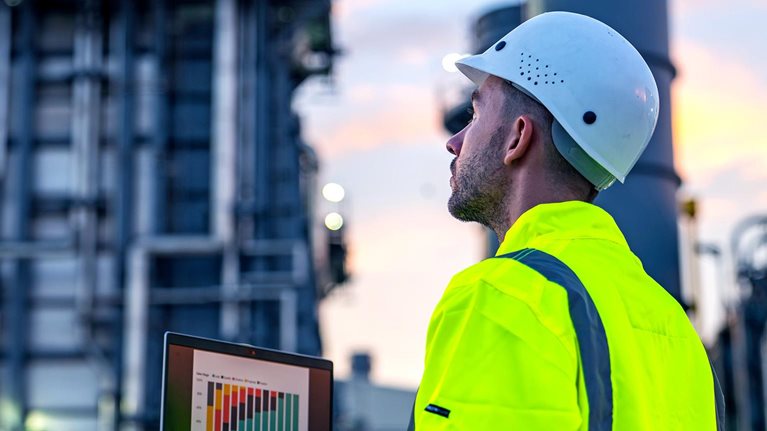 An industrial engineer using a laptop to monitor operational data at a facility.