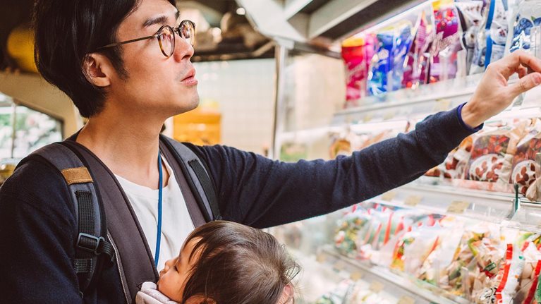 Handsome young dad carrying his baby in a baby carrier while shopping in a supermarket.