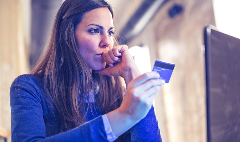 Image of a woman with a concerned look on her face shopping online and paying with card.