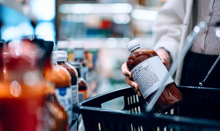 Close-up image of a woman putting a bottle into her shopping basket while shopping in a supermarket.