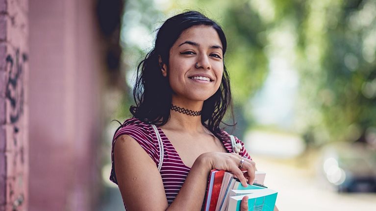 Young student woman standing on street and holding books.
