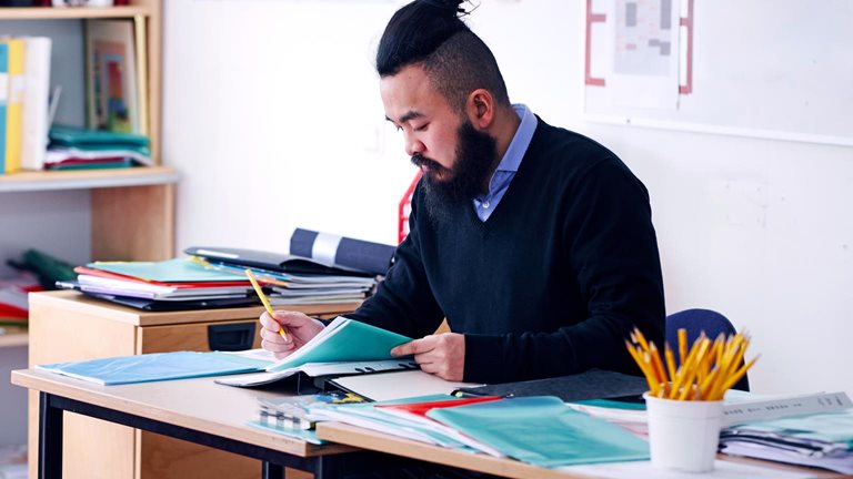 A teacher sitting at his desk looking at a booklet