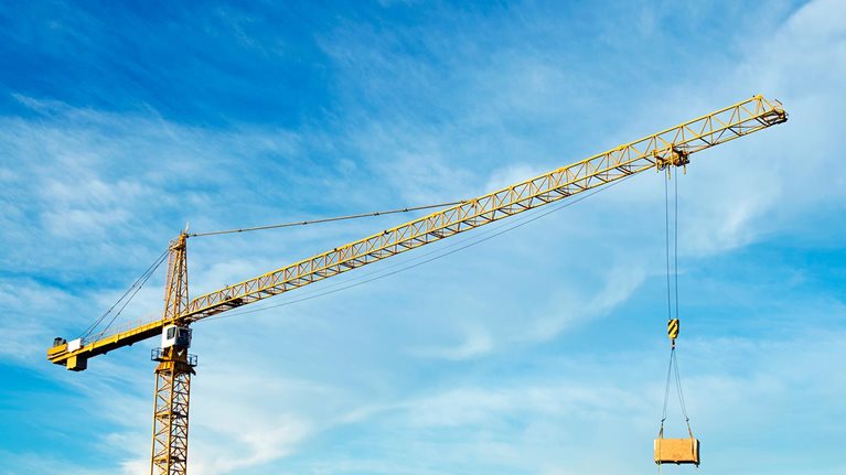 Crane at construction site against cloudy sky