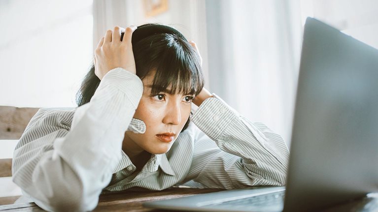 This image shows a person appearing stressed or frustrated while working on a laptop computer, representing professional challenges.