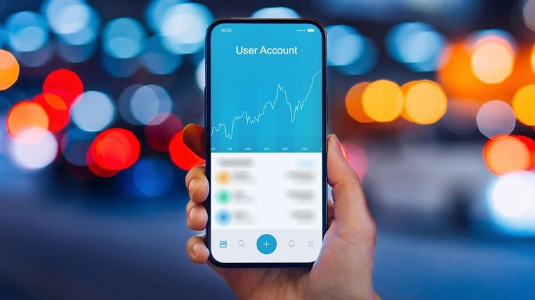 Woman's hand holding up smartphone against illuminated city street lights, using NFT investment wallet on smartphone in city, working with blockchain technologies.