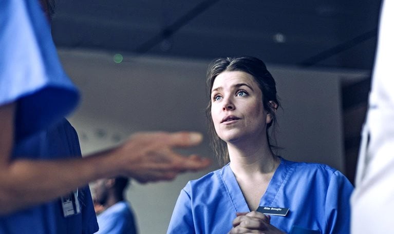 An attentive nurse, whose face shows a look of thoughtful consideration and slight apprehension, having a discussion with another nurse in a hospital hallway.