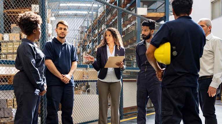 Female manager talking to a group of Latin American workers at a distribution warehouse.