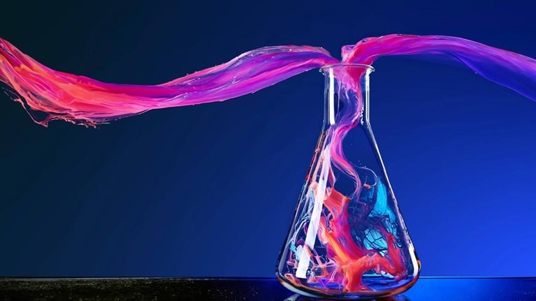 Image of colorful smoke gracefully swirling and mixing as it pours up and out of a vial.
