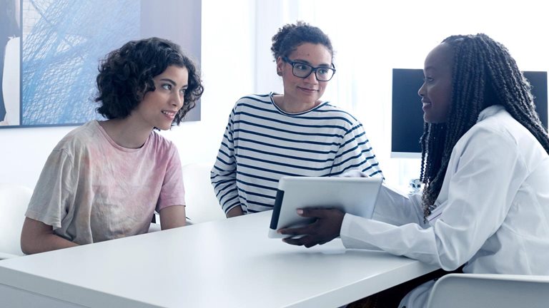 Female doctor telling mother and daughter medical results at doctors office using digital tablet