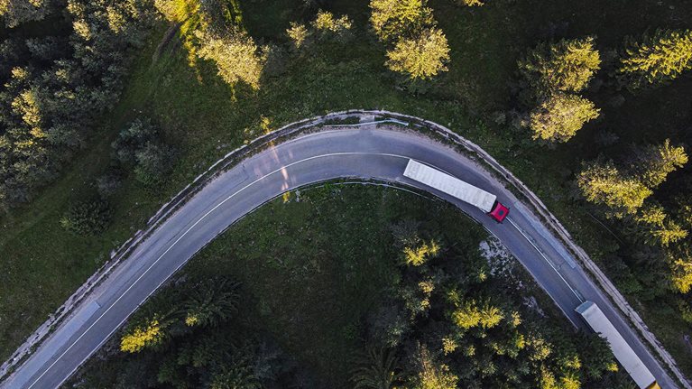 Drone point of view over two semi-trucks on a road curve in pine woodland.