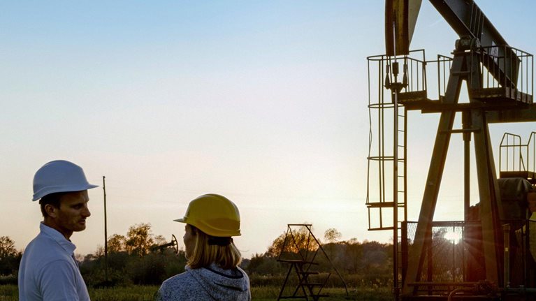 Two engineers standing near a pumpjack