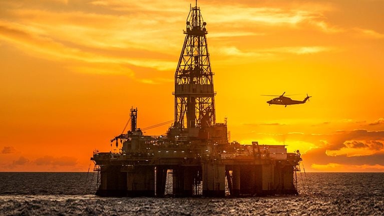 Helicopter flying over oil rig in sea against sky during sunset - stock photo