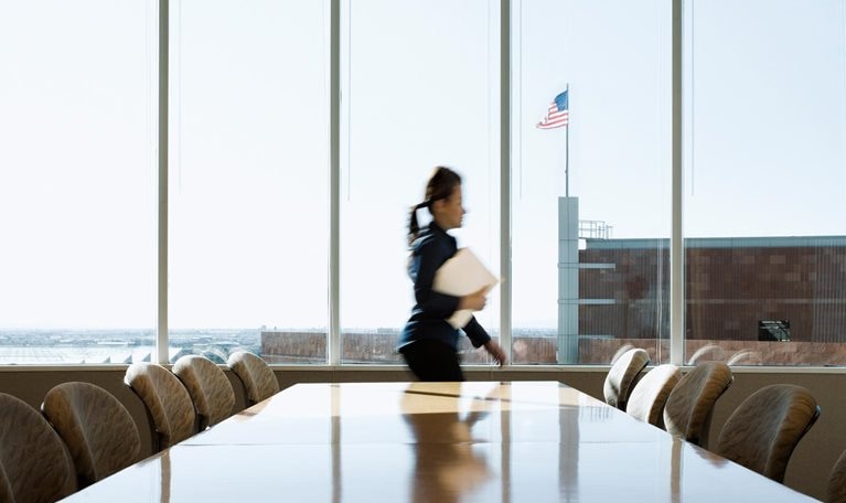 Hispanic businesswoman rushing through conference room, an American flag is seen though the window on top of an adjacent building