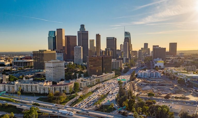 Drone view of downtown Los Angeles or LA skyline with skyscrapers and freeway traffic below.