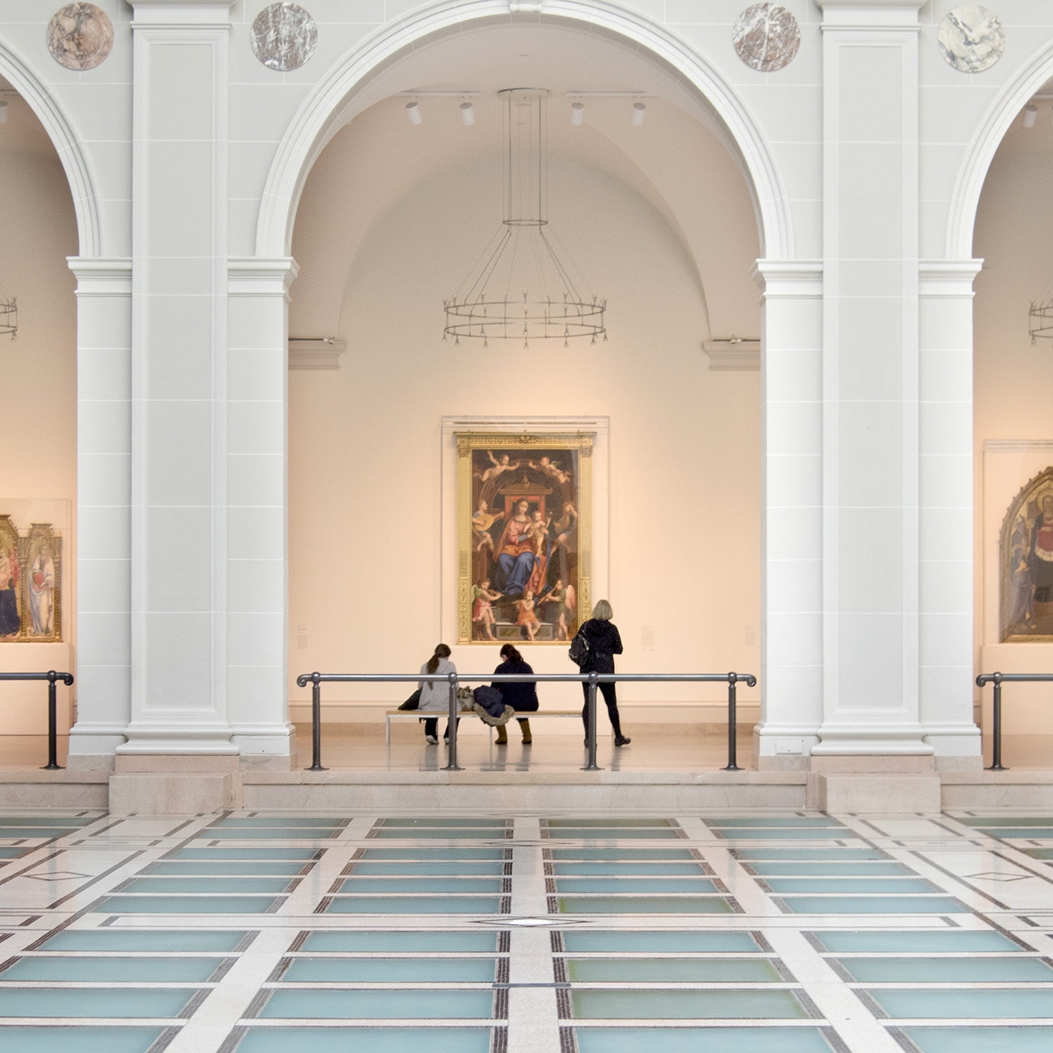 People view artwork along a hallway framed by three large arches in Brooklyn Museum’s Beaux-Arts Court.