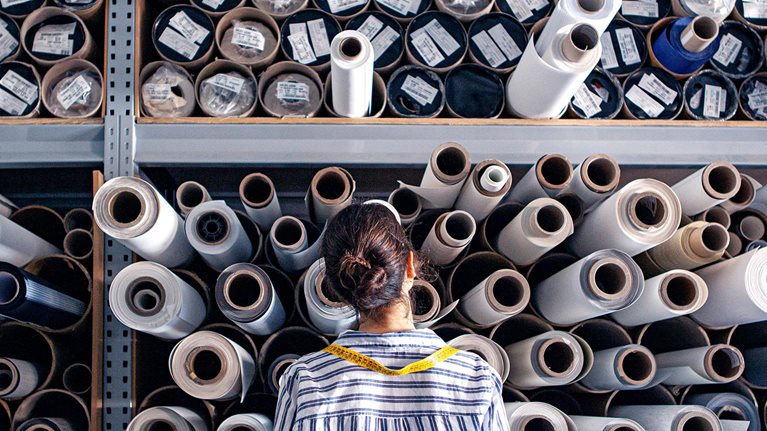 Portrait of textile designer choosing fabric from stack of rolls inside sustainable workshop.