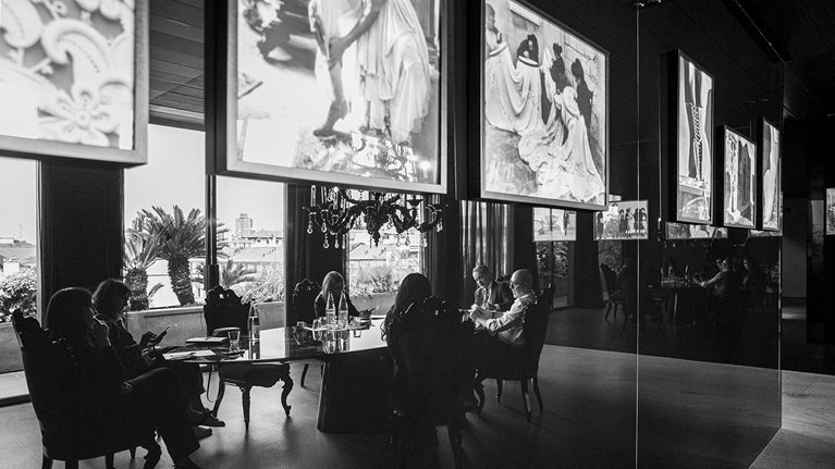 Executives sit around a long, oval table to discuss Dolce&Gabbana’s business, surrounded by images of the Italian brand’s artisans at work. 