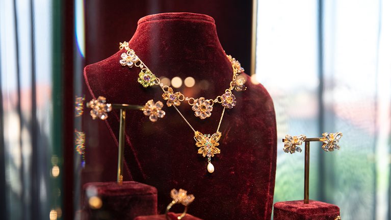 A Dolce&Gabbana matching fine jewelry set, including a floral-motif necklace, earrings, and rings, situated in a display case.