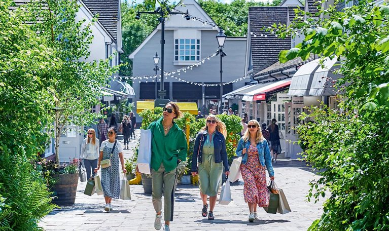 Shoppers carrying shopping bags walk outdoors through Bicester Village.