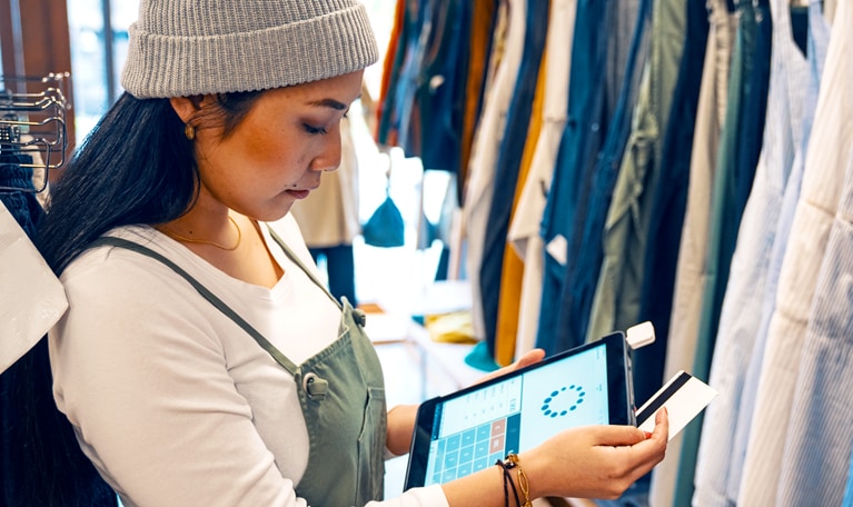 Retail shop clerk taking a mobile credit card payment on a digital tablet in a clothing boutique