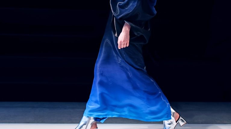 A woman struts down the runway in a creative blue designer satin dress