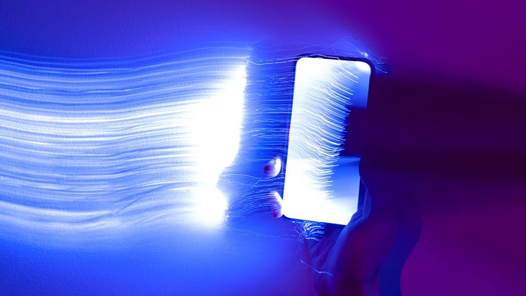 Close-up photo of a hand holding a mobile phone with light streaks trailing out of it.