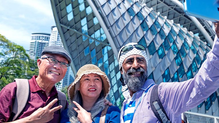 A senior Sikh tour guide and two senior Asian tourist taking selfie together in front the famous Saloma Bridge in the city of Kuala Lumpur.