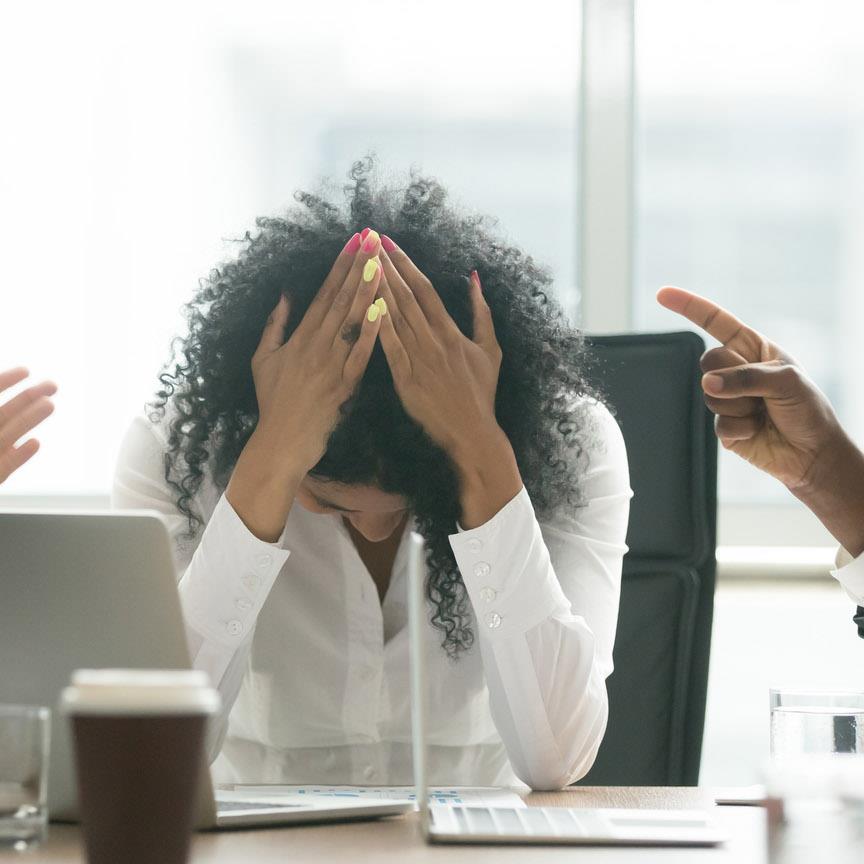 A woman with her hands over her head expressing frustration during a conference meeting with colleagues