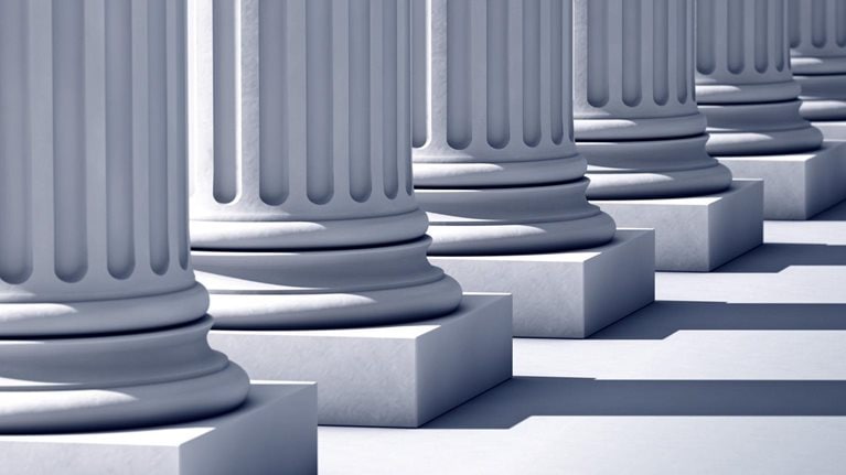 A deep row of stone columns with long linier shadows.