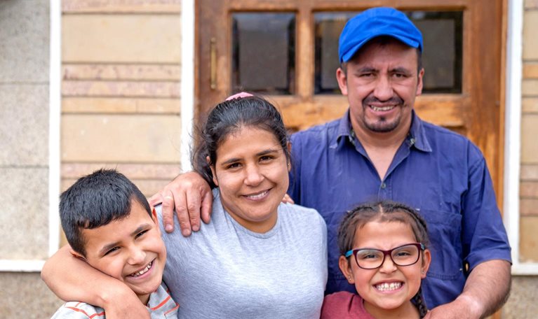 Portrait of a rural Latin American family in front of their new house and looking at the camera smiling