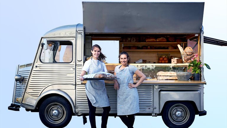 Image of confident women standing next to their vintage van that has been converted into a foot truck.