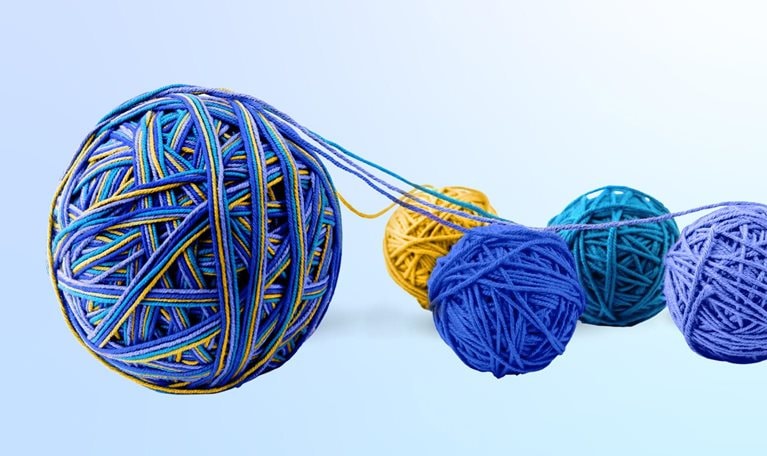 A large yarn ball composed of various hues, originating from four smaller yarn balls. The smaller balls come in diverse tones of blue, with one exception of yellow, and are positioned next to the larger ball.