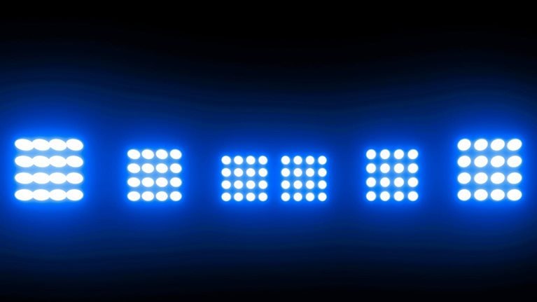 A row of five bright, white LED stadium lights are positioned against a dark blue backdrop.