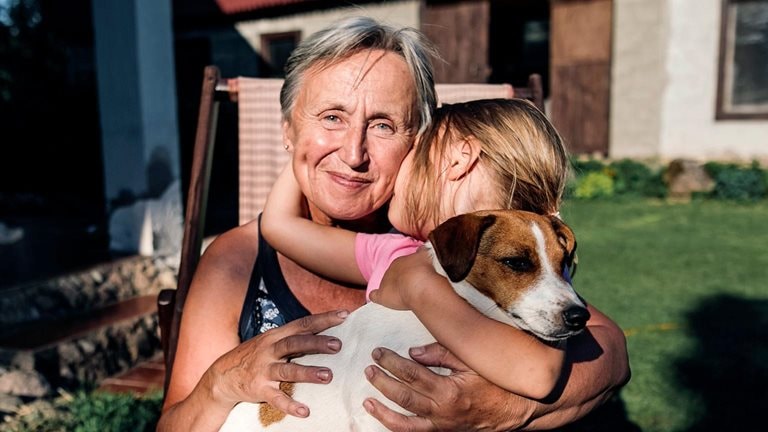 Smiling grandmother with granddaughter and dog on deckchair in garden