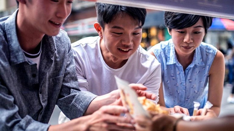 Three people ordering food at a street food counter