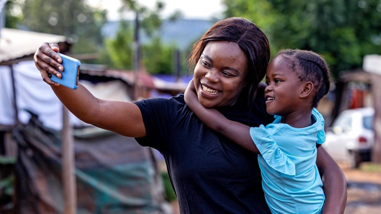 African woman holding her daughter taking a selfie in an informal settlement