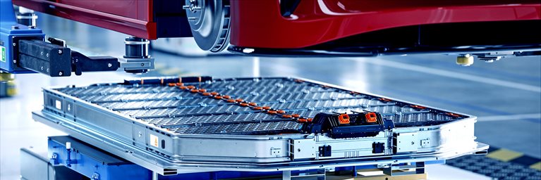 Image of an EV battery pack being assembled under an electric car on a production line, inside a modern factory.