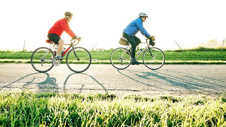 Wide shot of senior male friends on sunrise bike ride on rural road