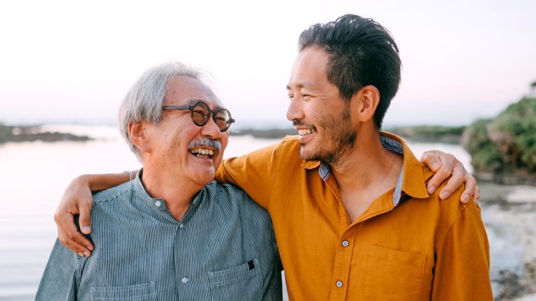 Senior father and adult son having a good time on beach at sunset