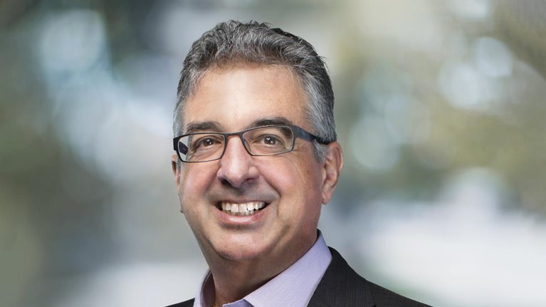 Portrait of a smiling Dimitri Christakis in a suit jacket and button down shirt against a blurred background of trees.