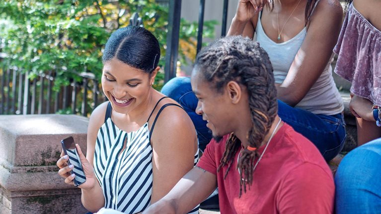 Group of Black friends together on the some stairs of a home, having fun looking at a mobile phone.